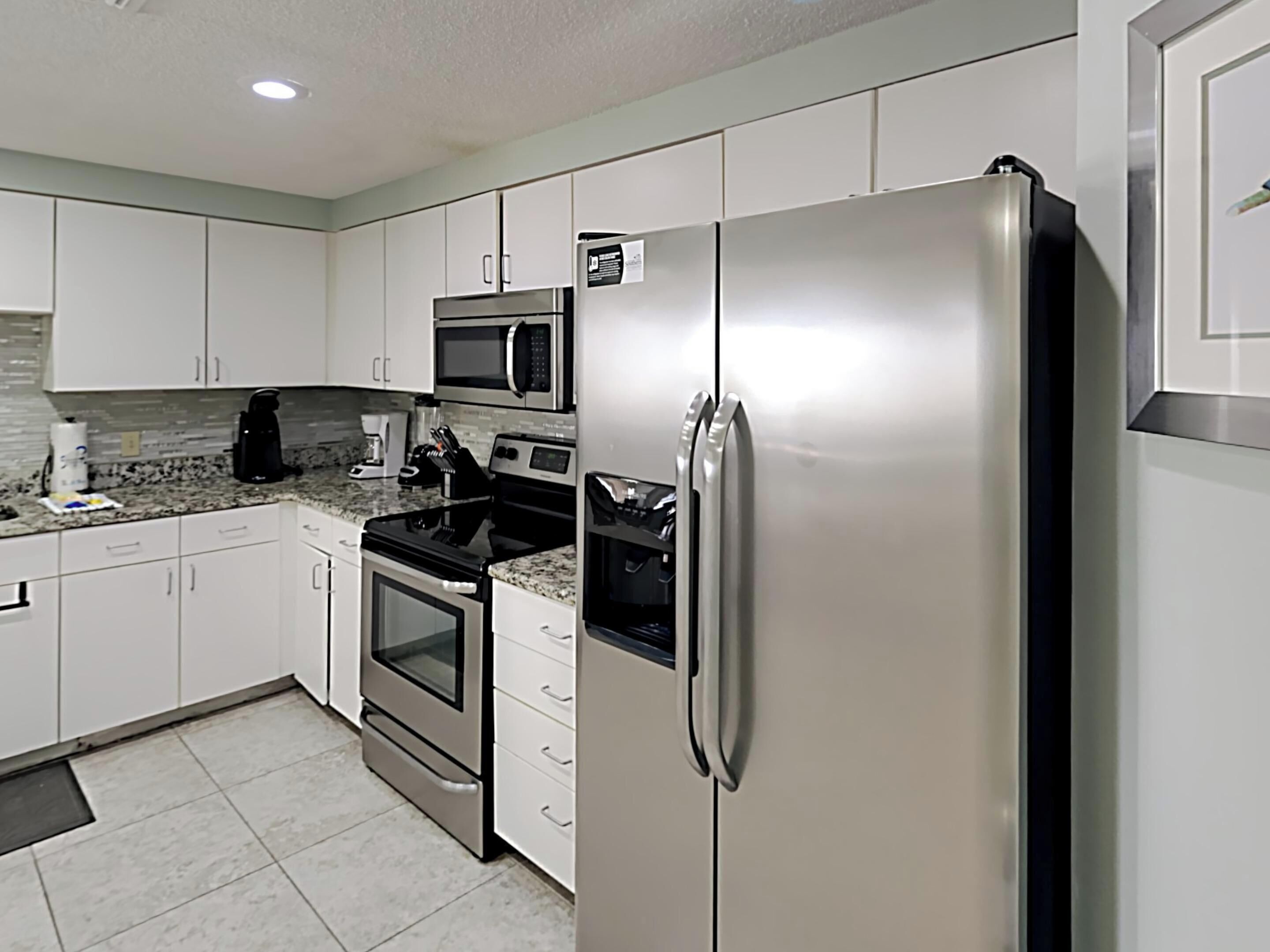A modern kitchen with stainless steel appliances, white cabinetry, and a tiled backsplash.