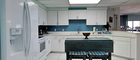Una cocina moderna con armarios blancos, salpicadero azul, una isla central con taburetes y un refrigerador a la izquierda.