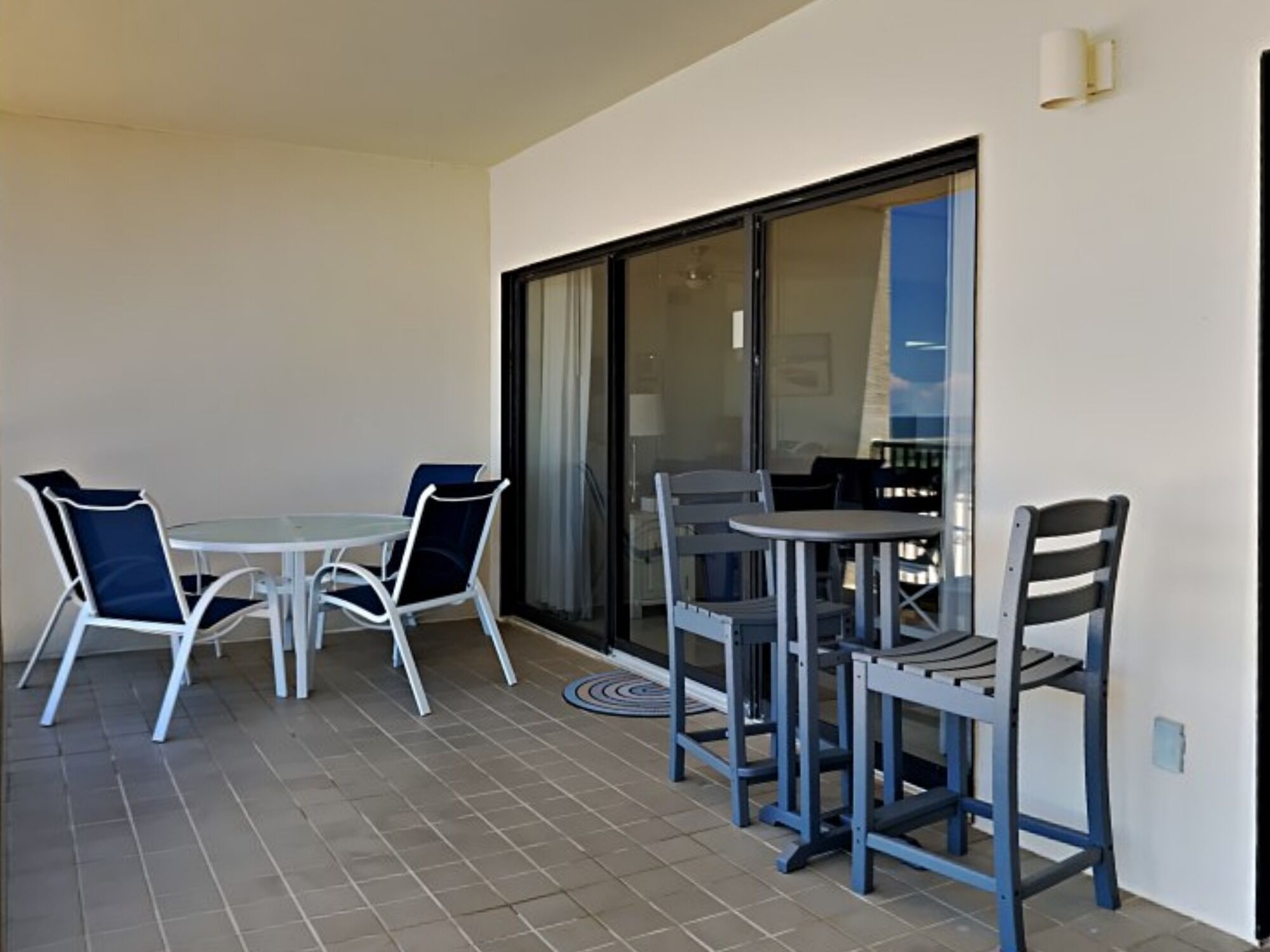 En balkon med et bord og stole, en skydedør og udsigt til en bygning.