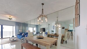 Un'ampia zona giorno con un tavolo da pranzo in legno, sedie bianche, un divano blu e un grande specchio che riflette l'ambiente.