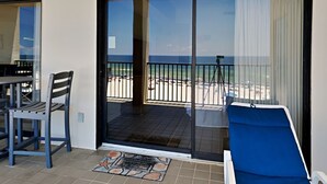 Un balcone con vista sulla spiaggia, un tavolo con sedie e un lettino prendisole.