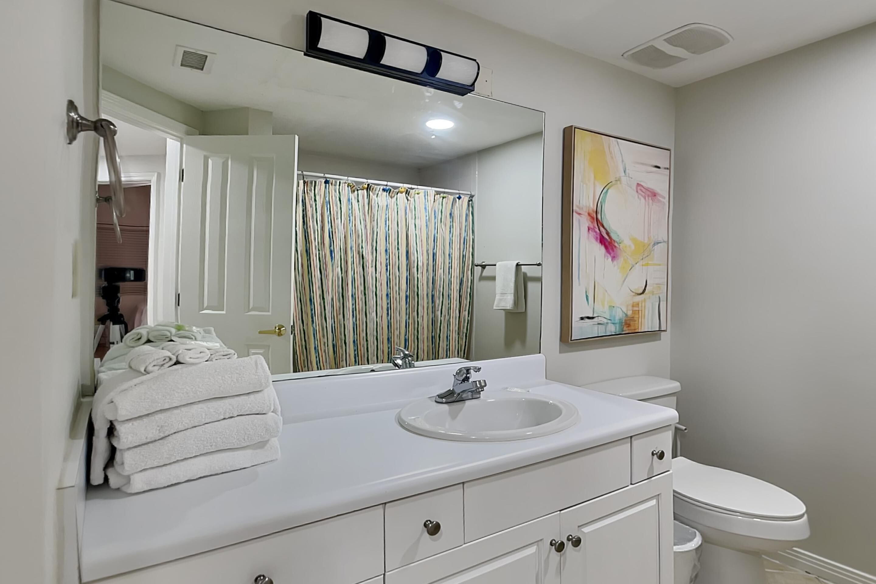 A bathroom with a white vanity, a sink, a toilet, a shower curtain, and a large mirror.