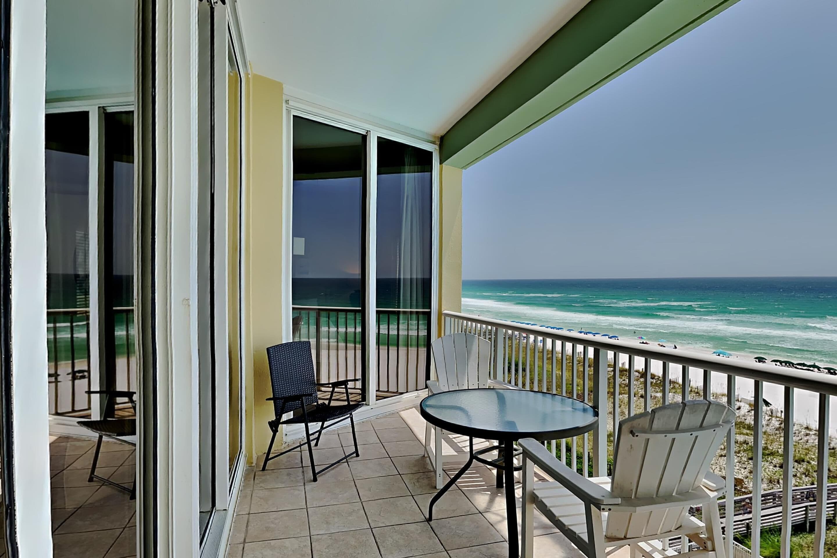 Ein Balkon mit Tisch und Stühlen, der Blick auf einen Strand mit dem Meer bietet.