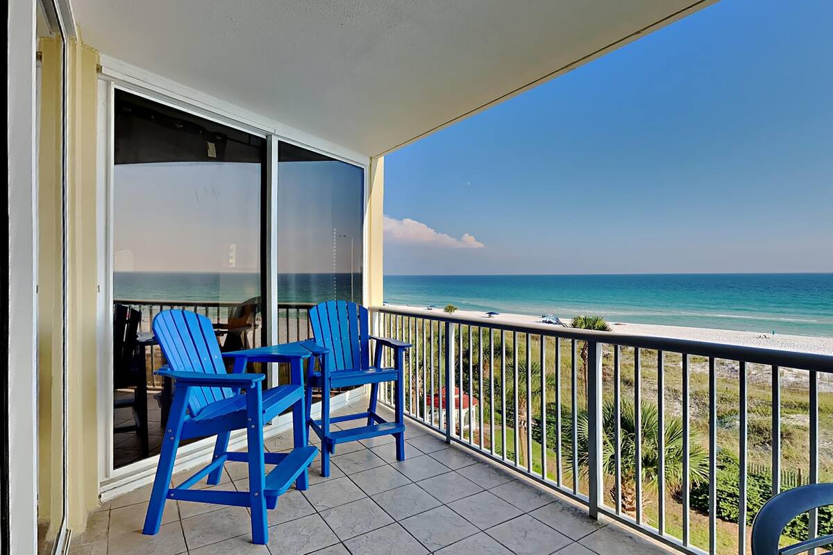 Un balcon avec deux chaises bleues, une porte vitrée et une vue sur la plage.