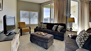 Ein Wohnzimmer mit einer Couch, einem Hocker und einem Sessel, einem Fernseher und einem Deckenventilator.