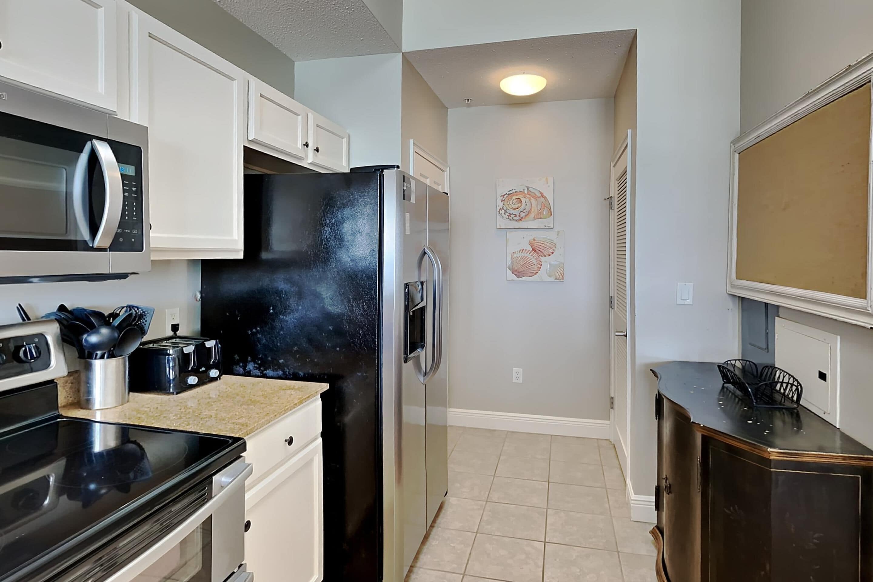 A kitchen with white cabinets, a black refrigerator, a microwave, and a stove. There are two framed pictures on the wall.