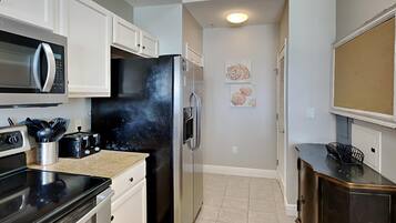 A kitchen with white cabinets, a black refrigerator, a microwave, and a stove. There are two framed pictures on the wall.
