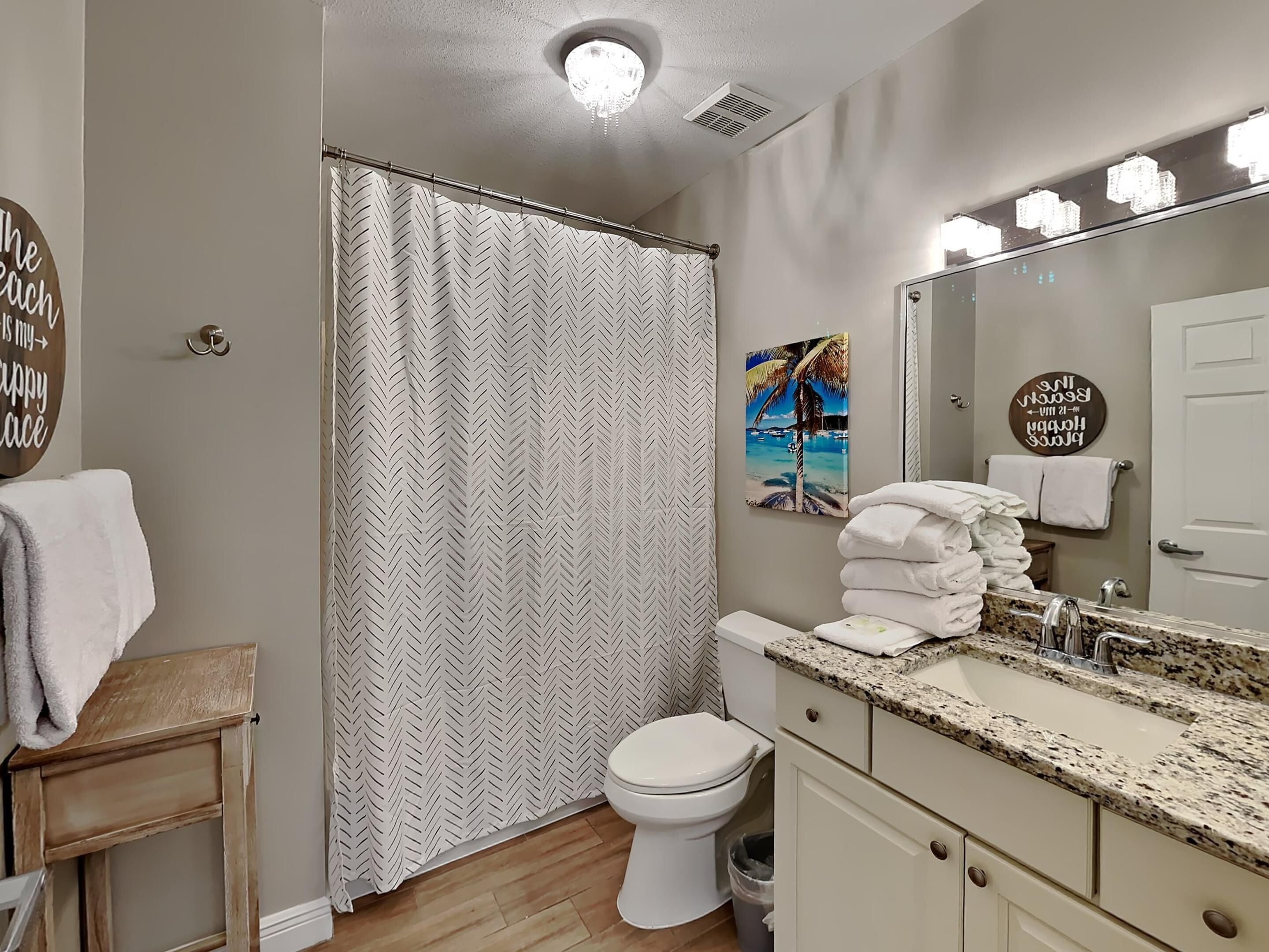 A bathroom with a shower curtain, toilet, sink with a mirror, and towels.