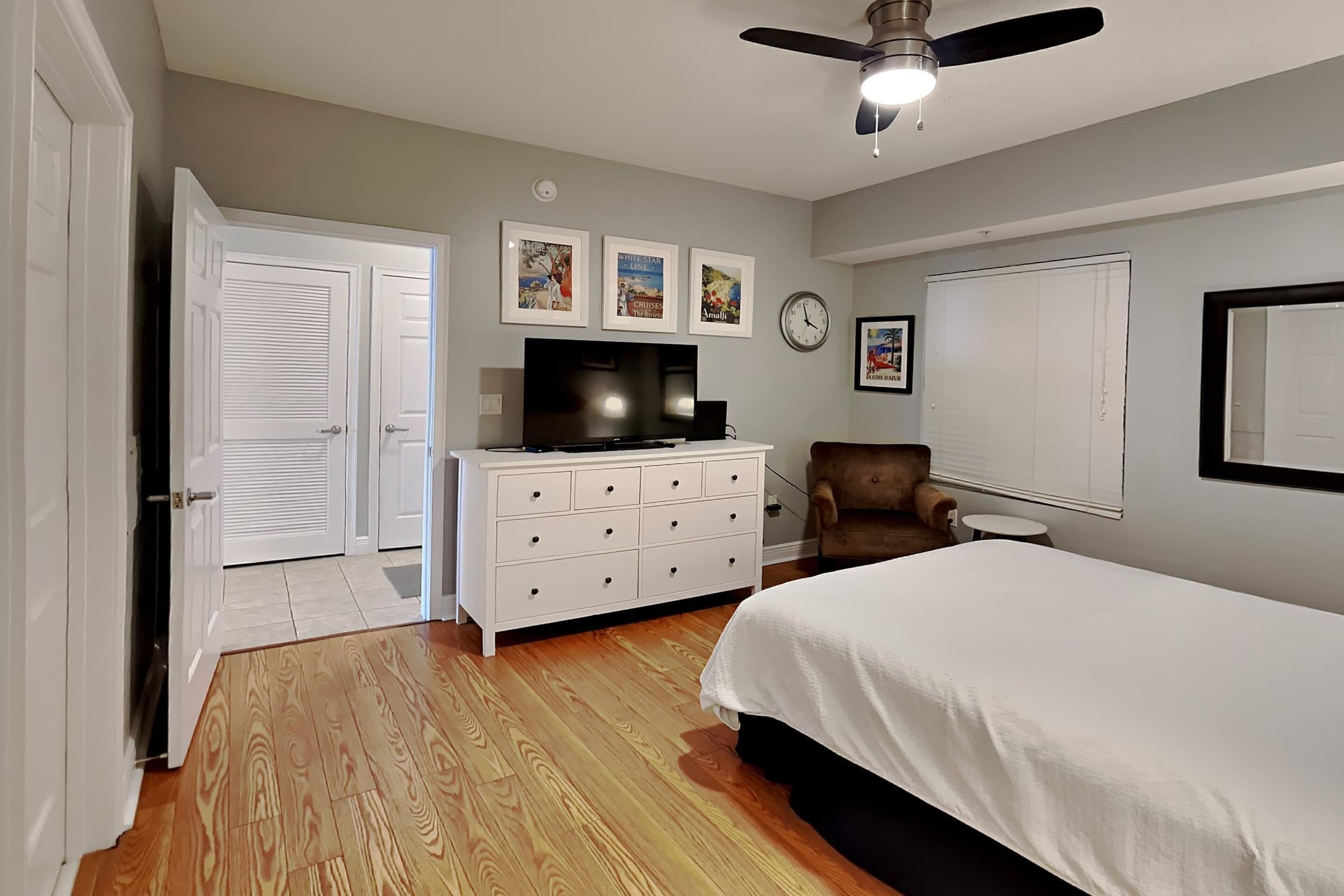 Une chambre à coucher avec un lit, une commode, un téléviseur, une chaise et une horloge au mur.