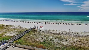 Ein Strand mit einer Holzpromenade, die zum Ufer führt, feinem Sand, Sonnenschirmen und dem Meer im Hintergrund.