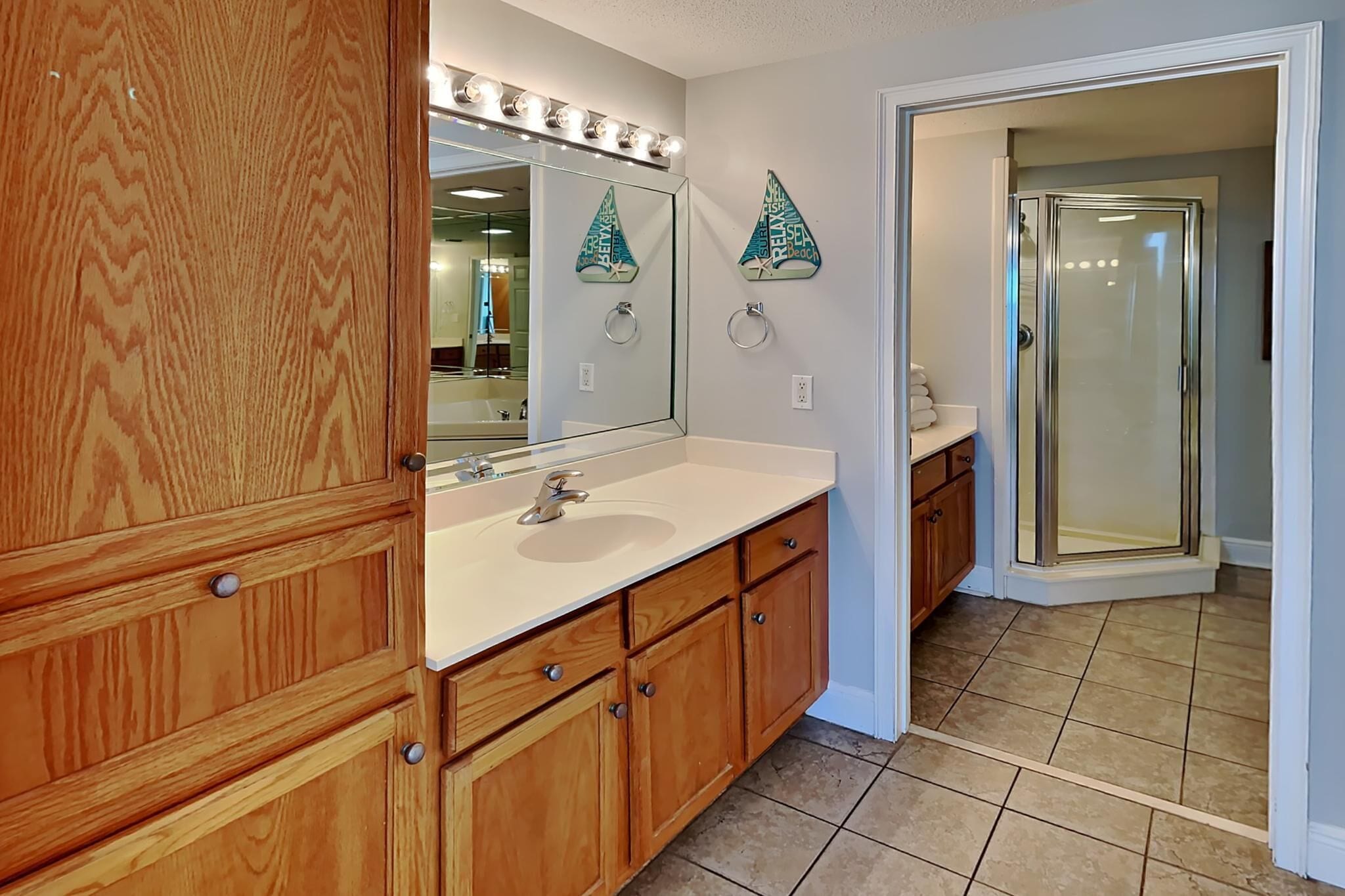 A bathroom with wooden cabinetry, a large mirror, and a glass shower enclosure.
