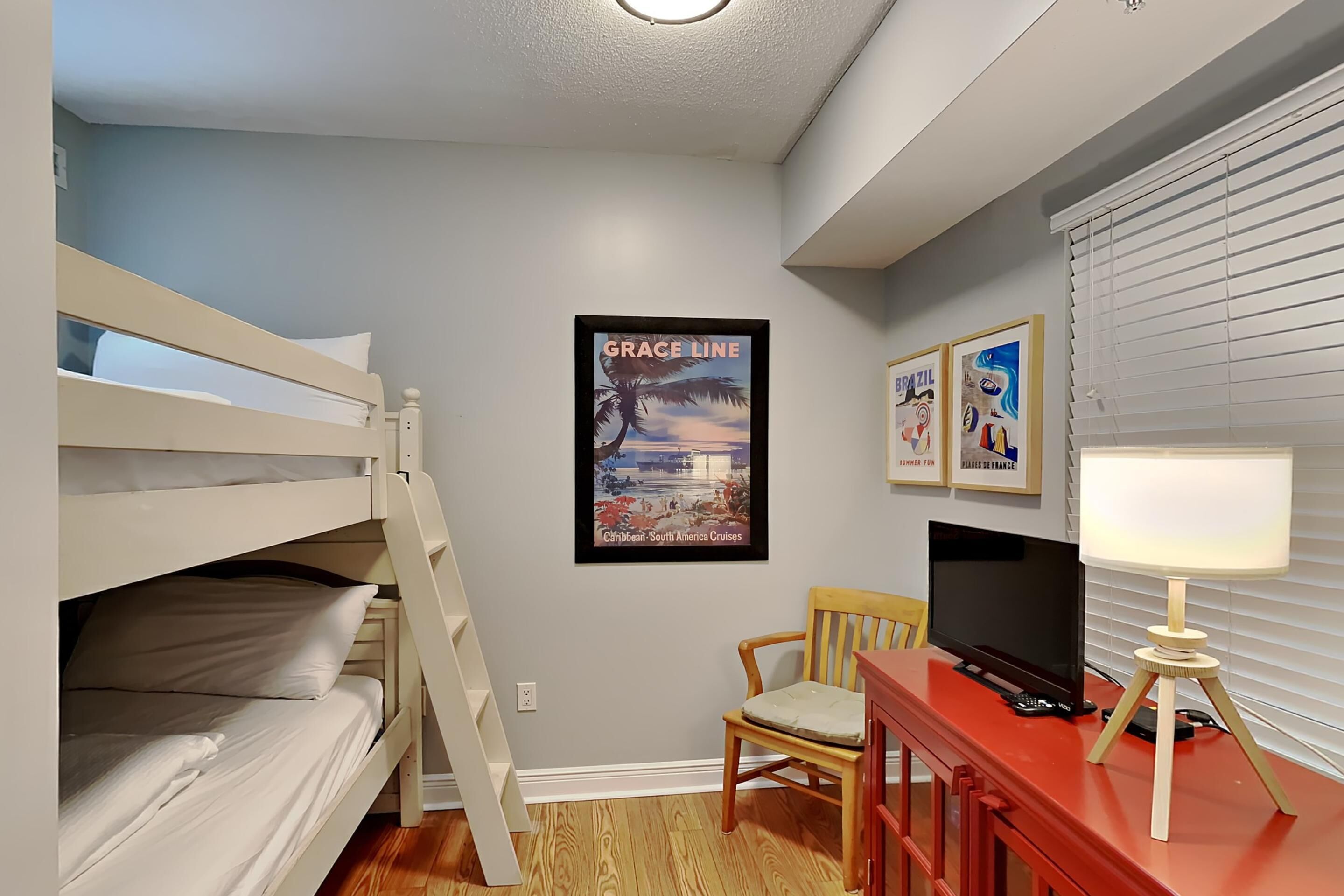 A bedroom with bunk beds, a desk with a TV, a chair, and a poster on the wall.