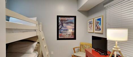 A bedroom with bunk beds, a desk with a TV, a chair, and a poster on the wall.