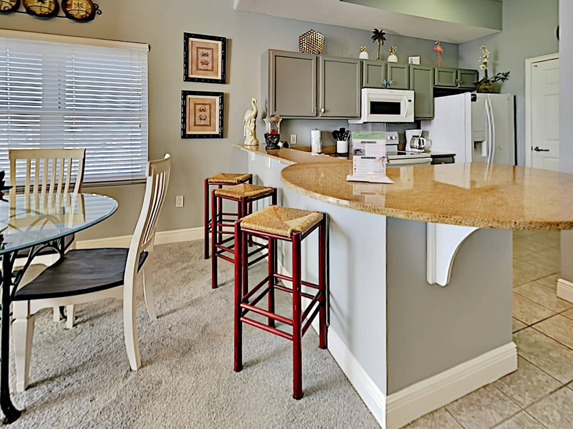 A kitchen with a central island, bar stools, a dining table with chairs, and a microwave.