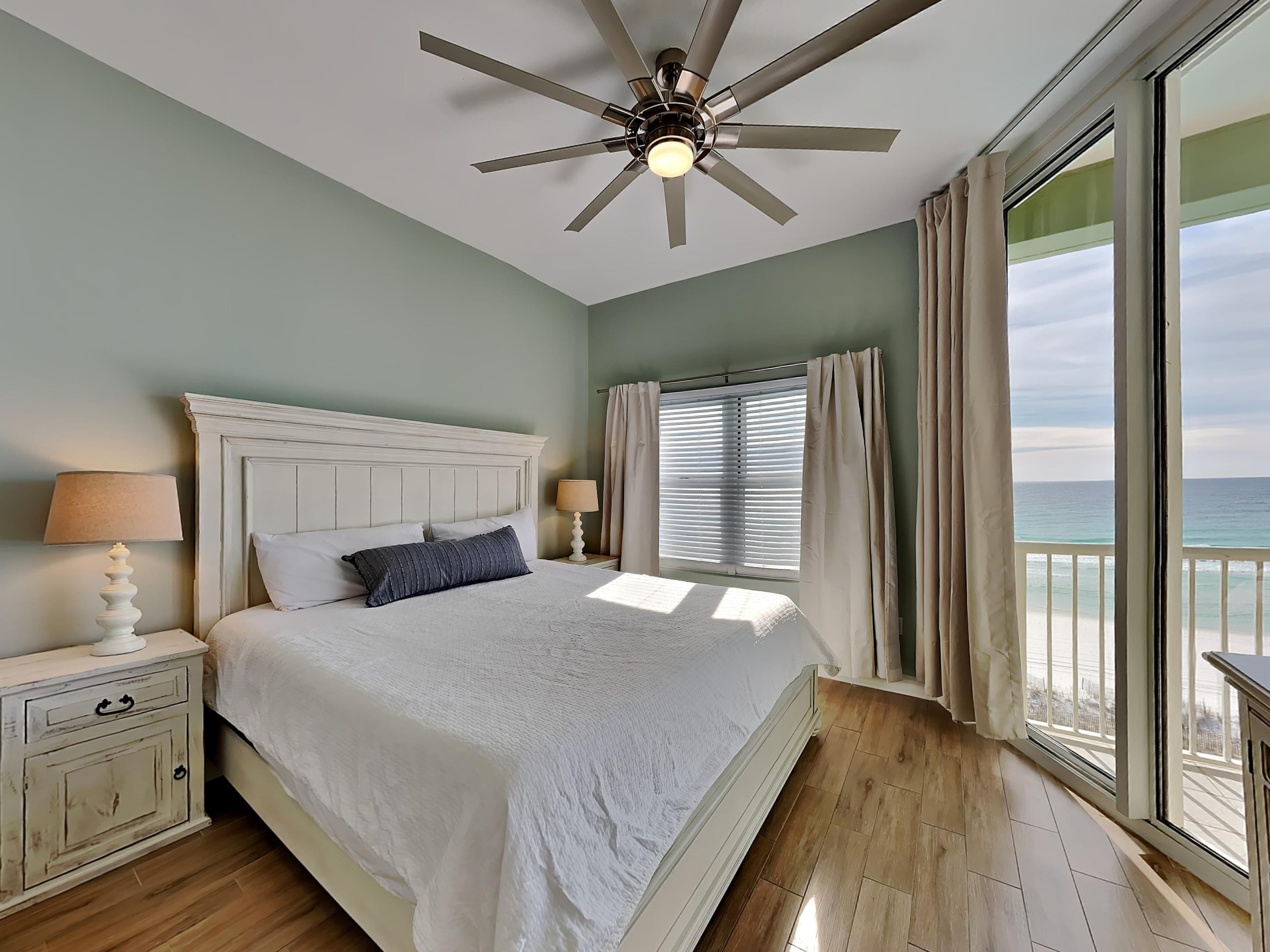 A bedroom with a bed, nightstands, a ceiling fan, and a view of the ocean.