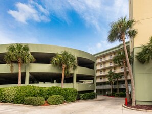 A multi-story parking garage with a curved design, surrounded by palm trees and well-maintained hedges. - Water's Edge by Southern Vacation Rentals (Fort Walton Beach)