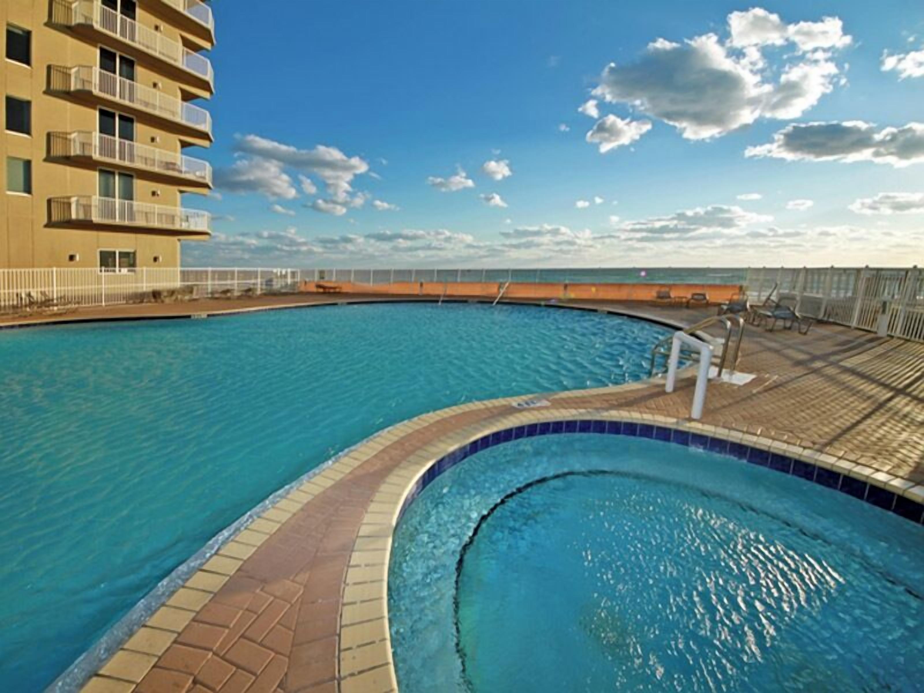 A swimming pool with a curved edge, a tiled deck, and a view of the ocean.