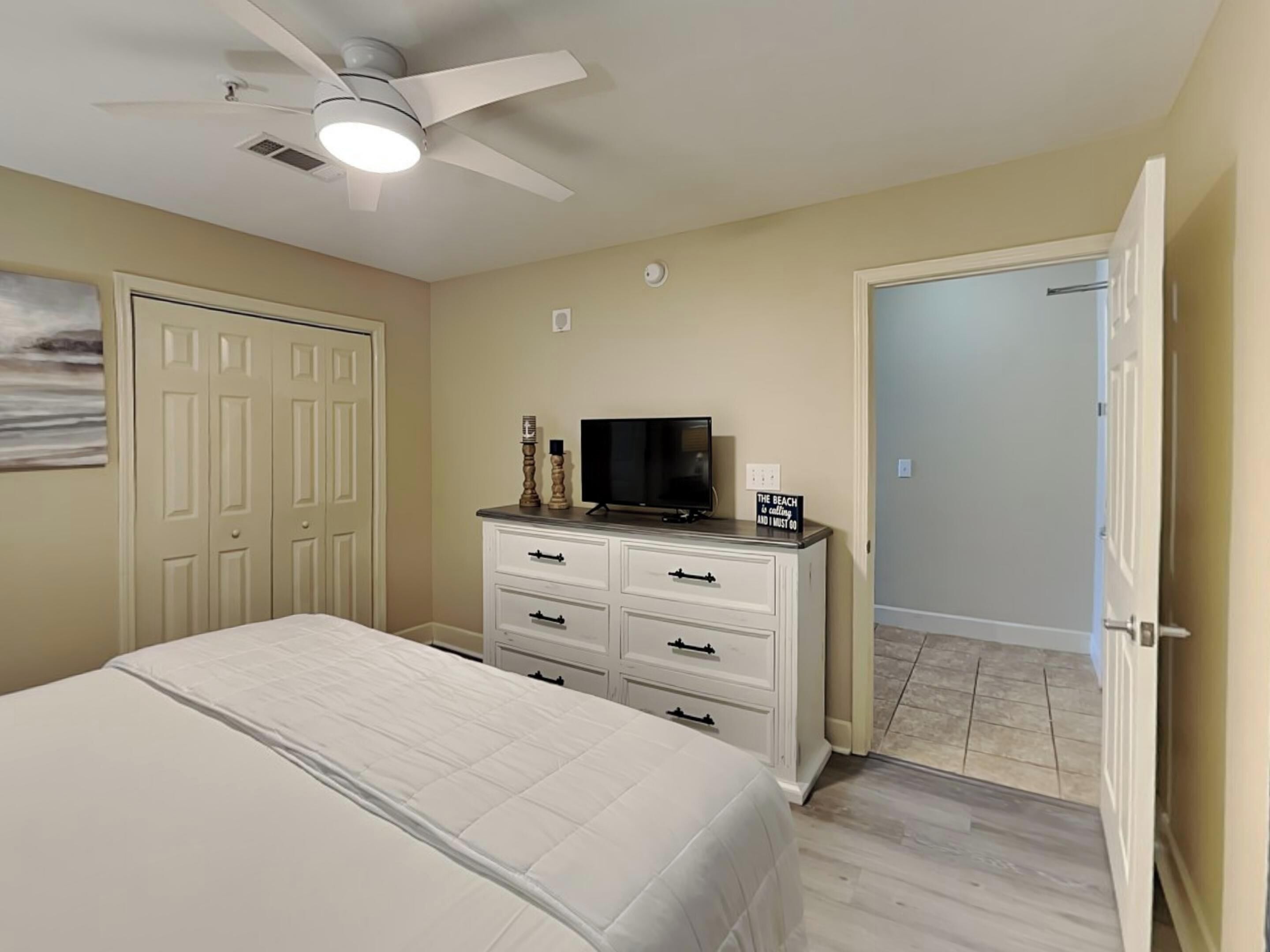 A bedroom with a bed, a dresser, a television, and a ceiling fan.