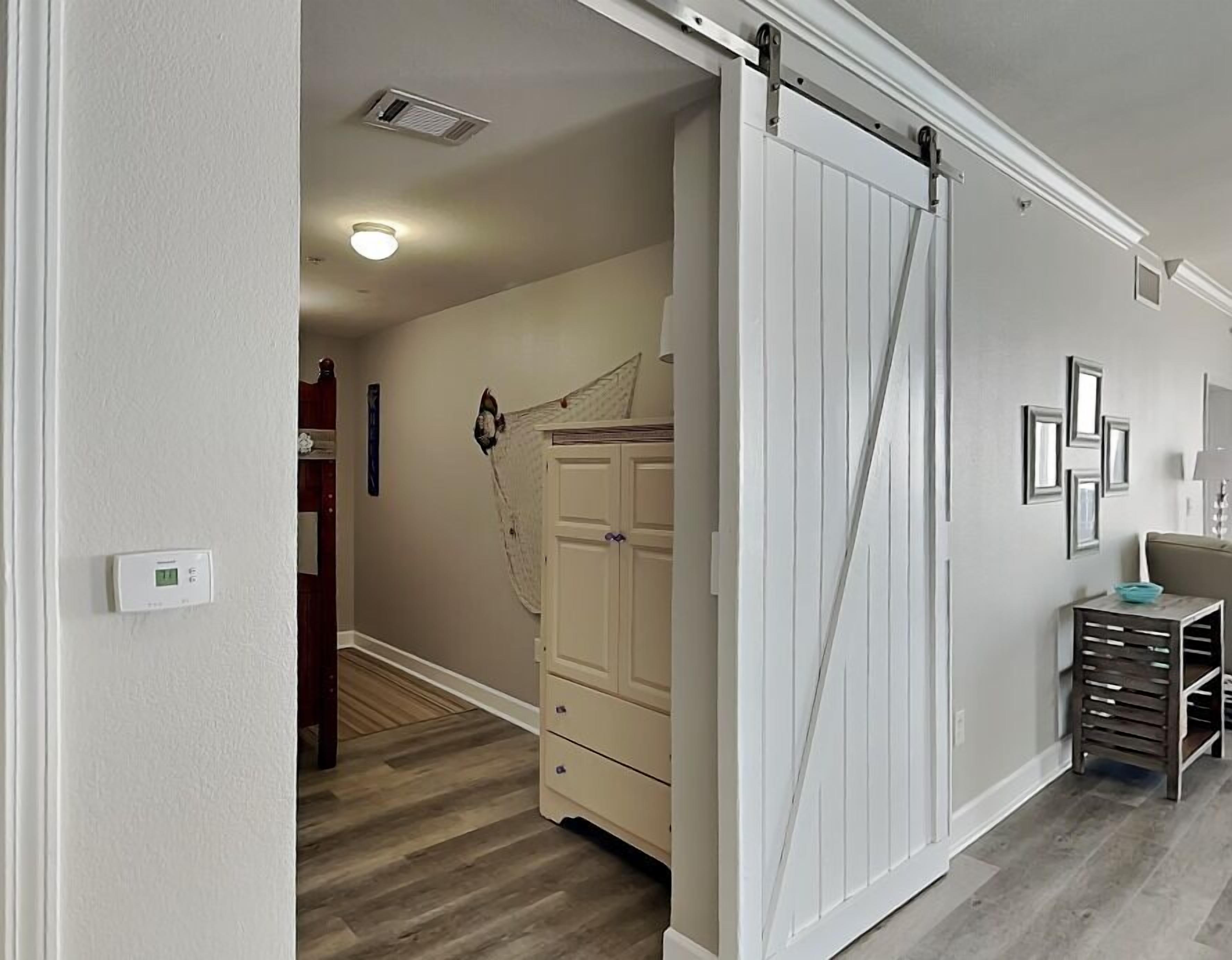 Une pièce avec une porte coulissante de style grange, une commode blanche, une petite table avec un bol, et une étagère fixée au mur.