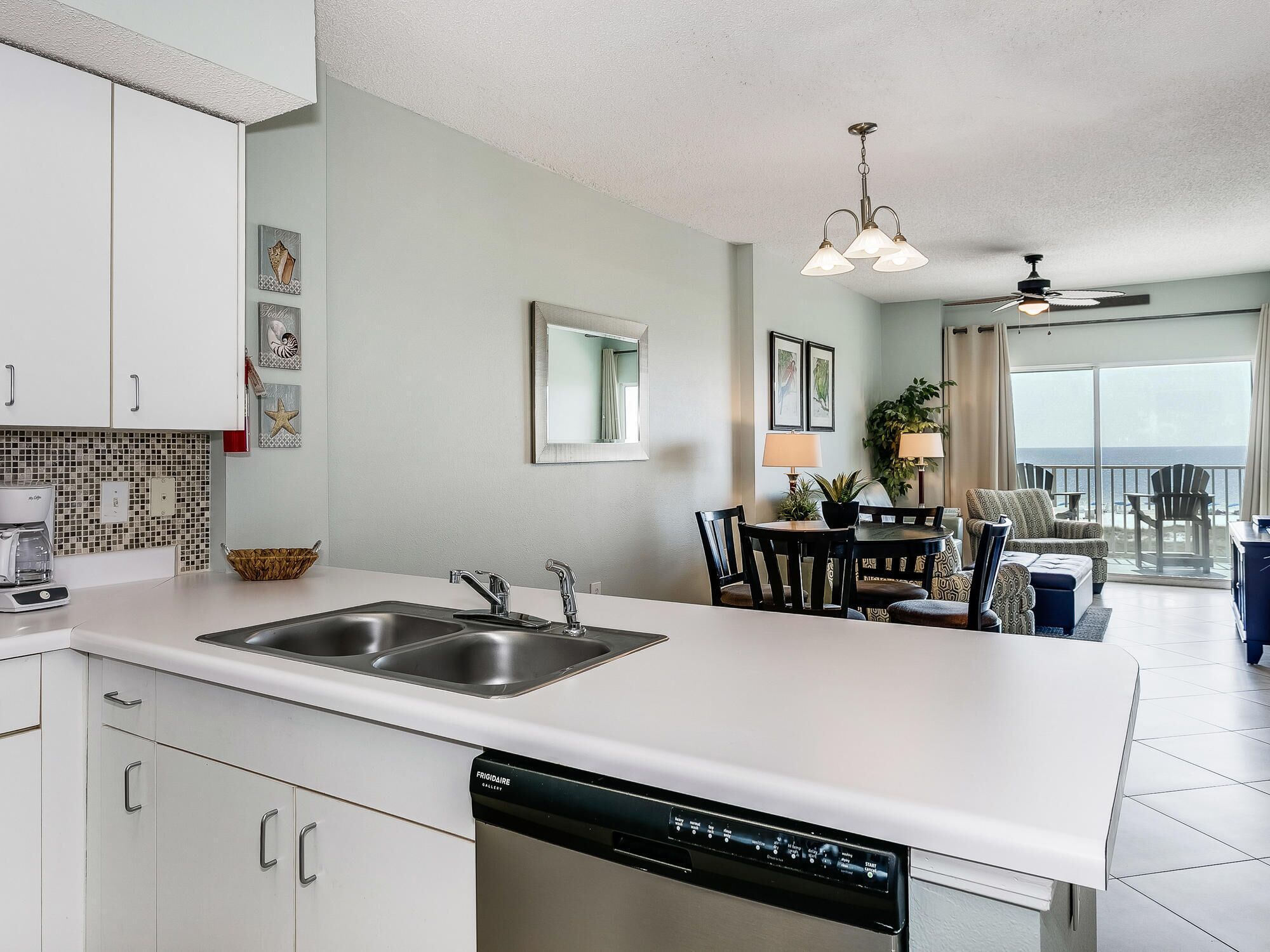 A modern kitchen with a dishwasher, a dining area with a table and chairs, and a view of the ocean through large windows.