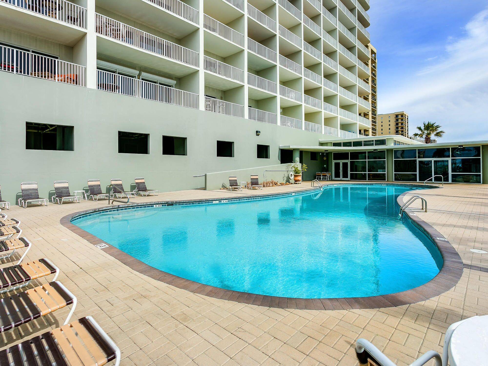 A swimming pool with lounge chairs and a building with balconies in the background.