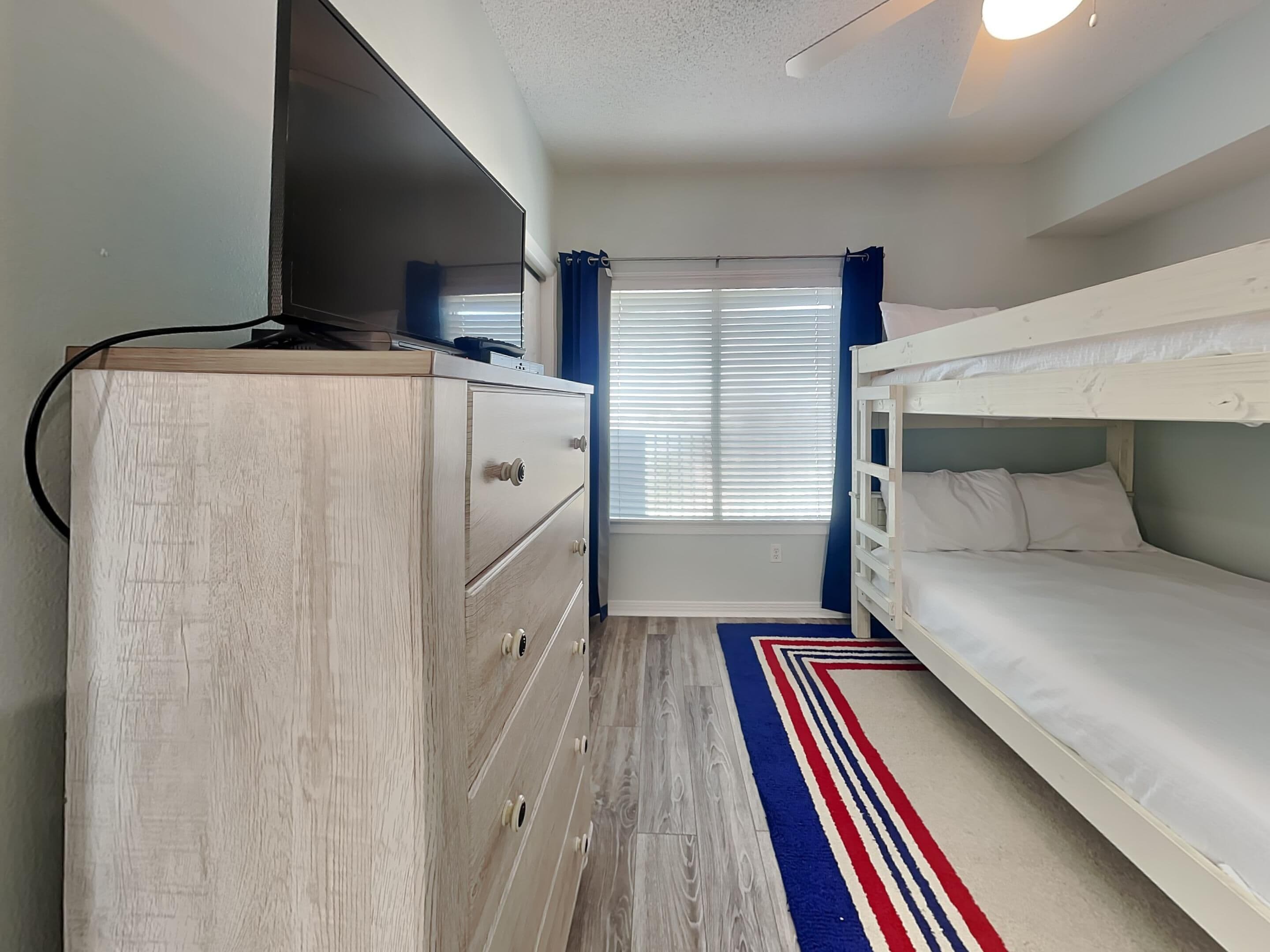 Una habitación con una cama litera, un aparador de madera y una ventana con persianas.