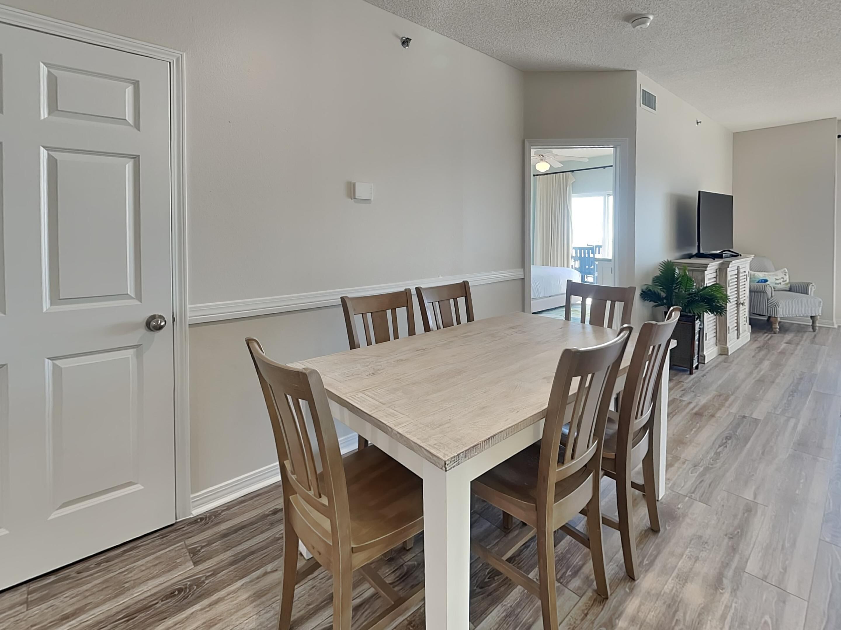 A dining area with a wooden table and chairs, a television, and a plant.