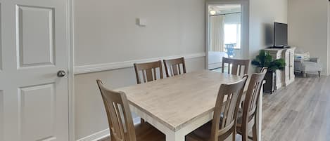 A dining area with a wooden table and chairs, a television, and a plant.