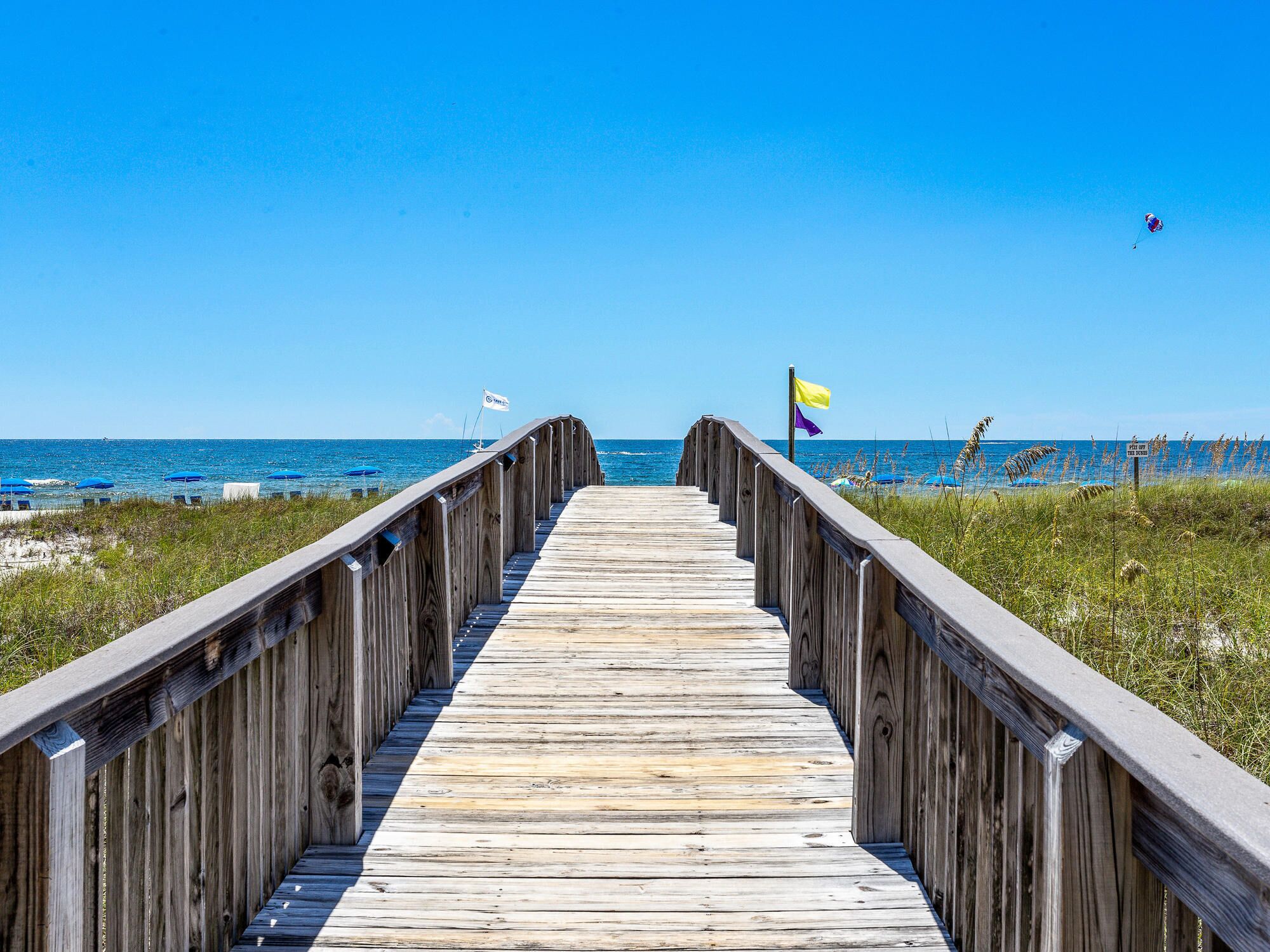 A wooden boardwalk leading to a beach with flags and umbrellas.