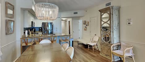 A spacious dining area with a wooden table and chairs, a chandelier, and a view into the kitchen.