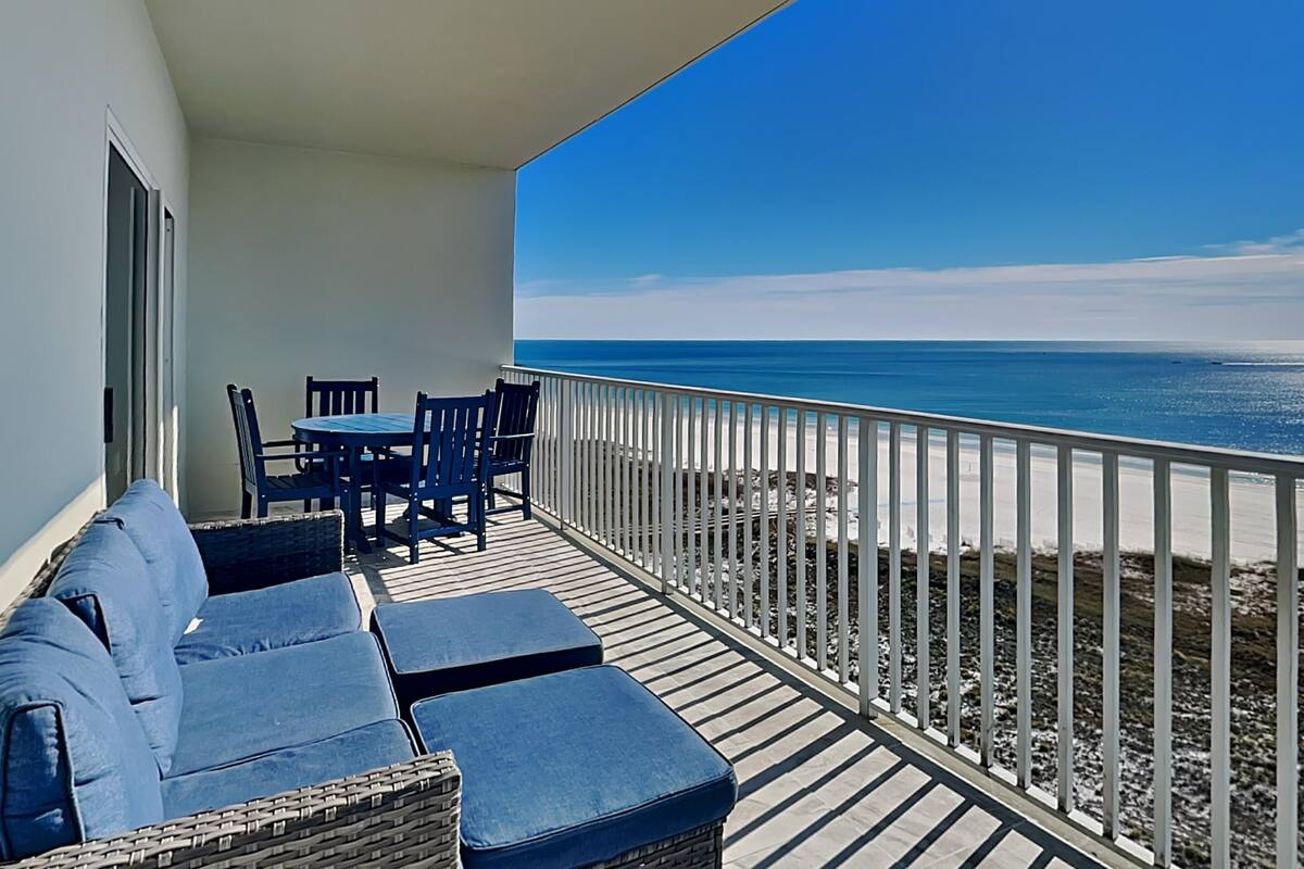 A balcony with a view of the ocean, a table with chairs, and a sofa.