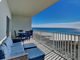 A balcony with a view of the ocean, a table with chairs, and a sofa.