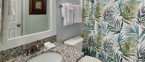 A bathroom with a granite sink, white toilet, and a shower curtain with a leaf pattern.