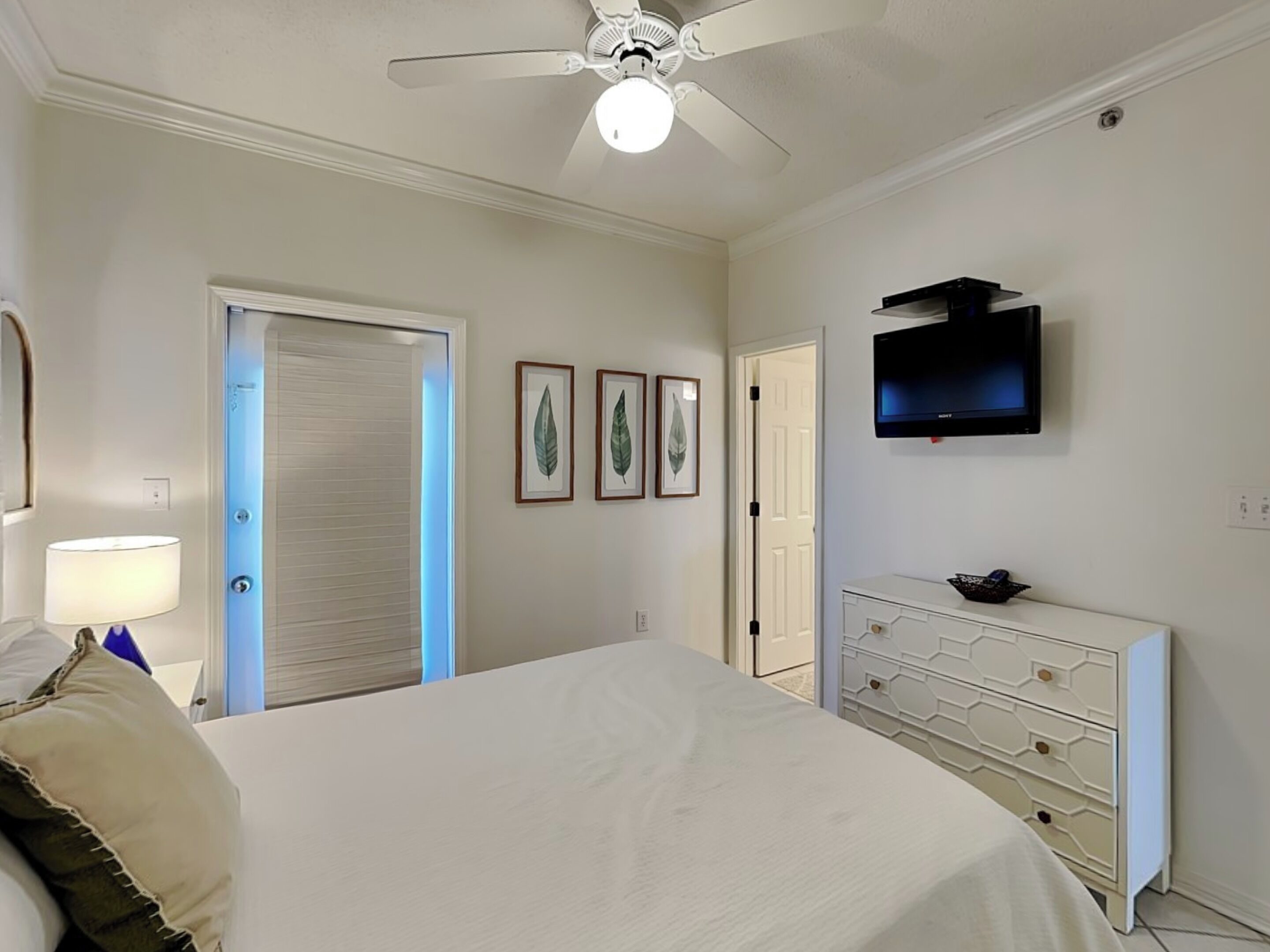 Een slaapkamer met een bed, een dressoir, een plafondventilator, een televisie en lijstjes met foto’s aan de muur.