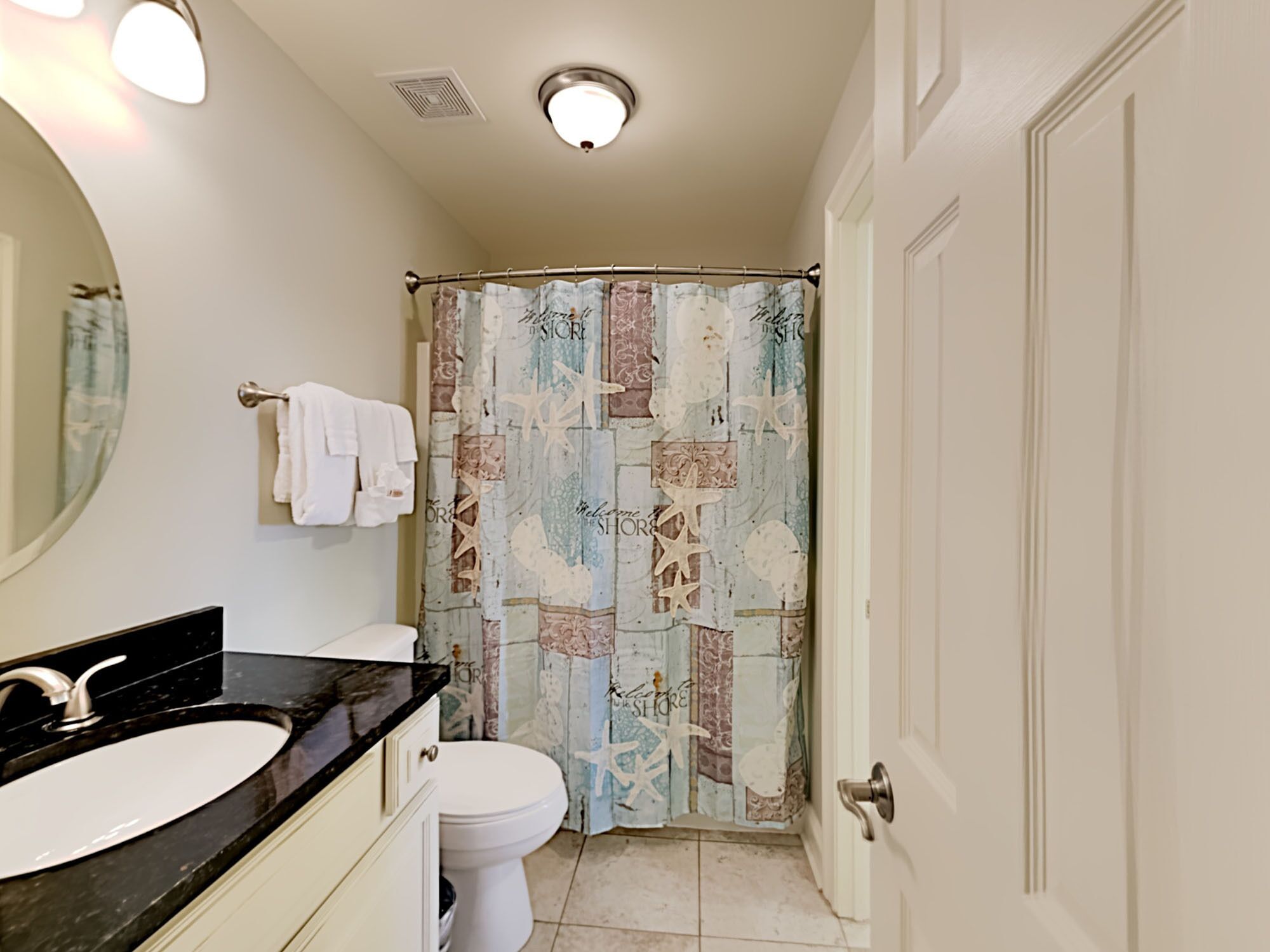 Une salle de bain avec un lavabo sur un plan de toilette noir, des toilettes blanches et un rideau de douche à motifs nautiques.