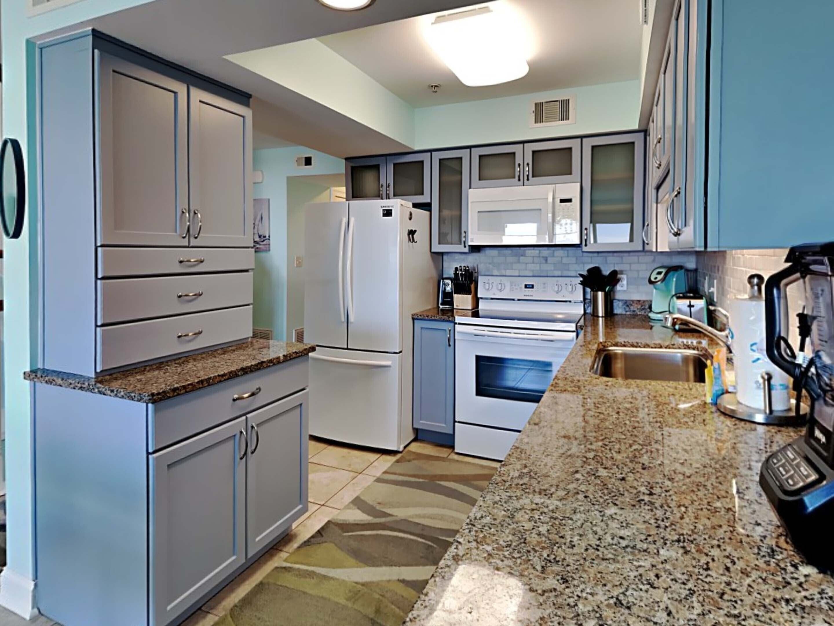 A kitchen with light blue cabinets, a granite countertop, a white refrigerator, a stove, and a coffee maker.