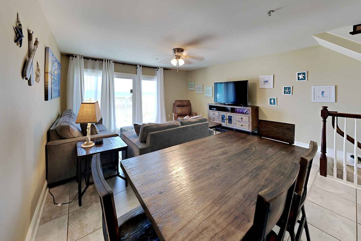 A spacious living room with a wooden dining table, a sofa, a TV, and a ceiling fan.
