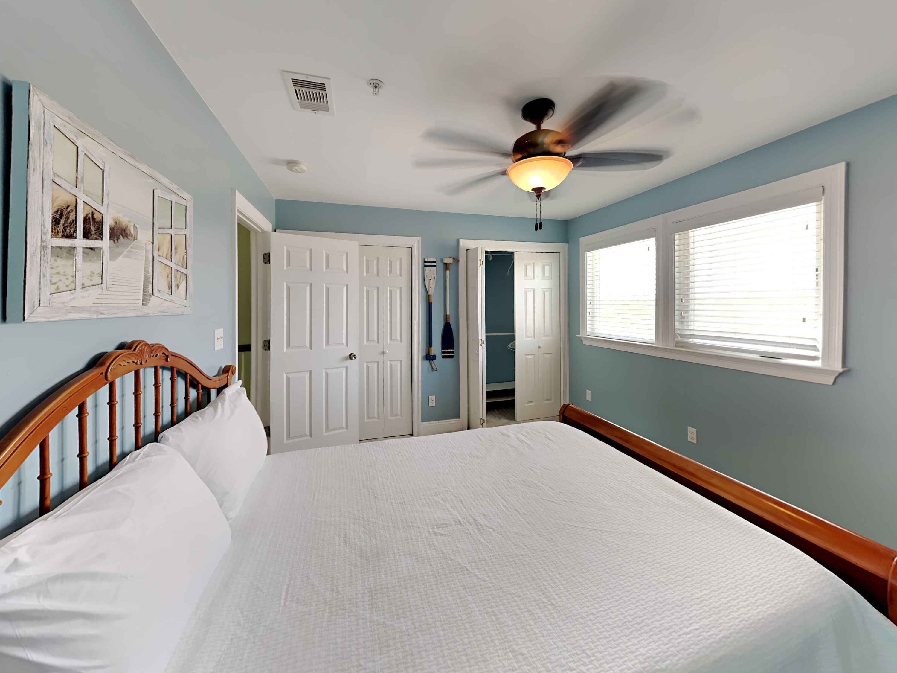 Une chambre à coucher avec un grand lit, un ventilateur de plafond, une fenêtre avec des stores et une porte donnant sur un placard.