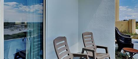 A balcony with two beige chairs, a small round table, and a glass door leading to a pool.