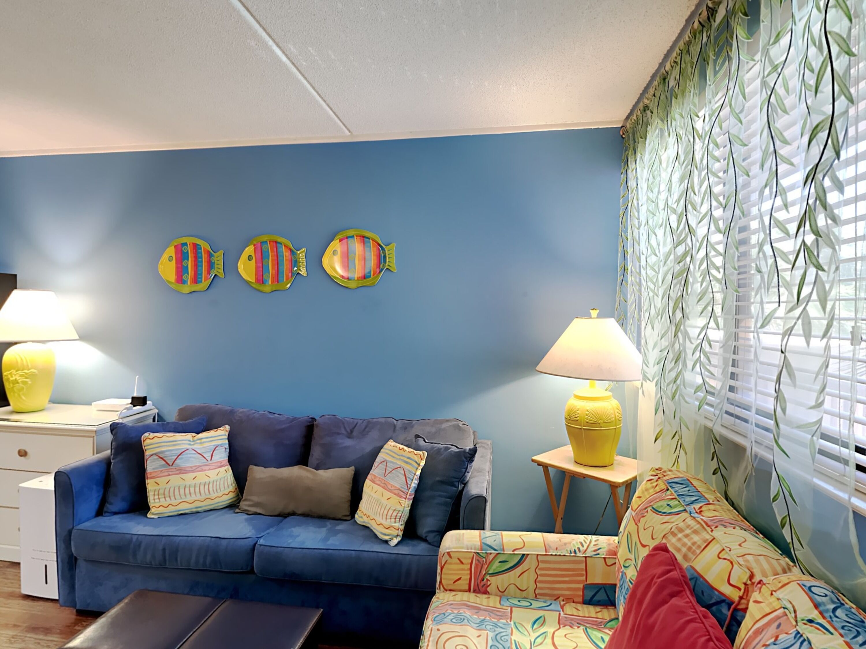 A living room with a blue sofa, two lamps, and decorative fish wall art.