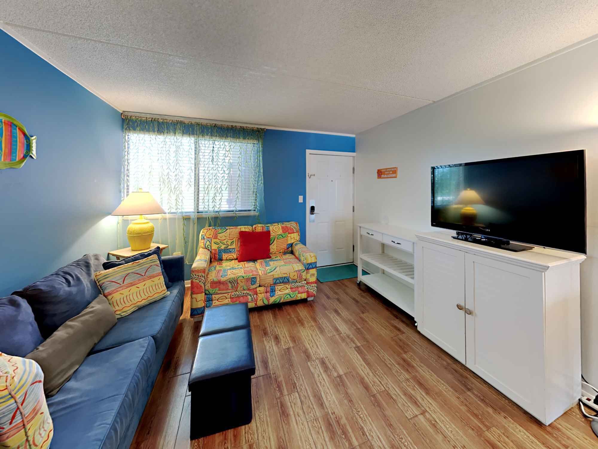 A living room with a blue sofa, colorful patterned sofa, and a television on a white cabinet.