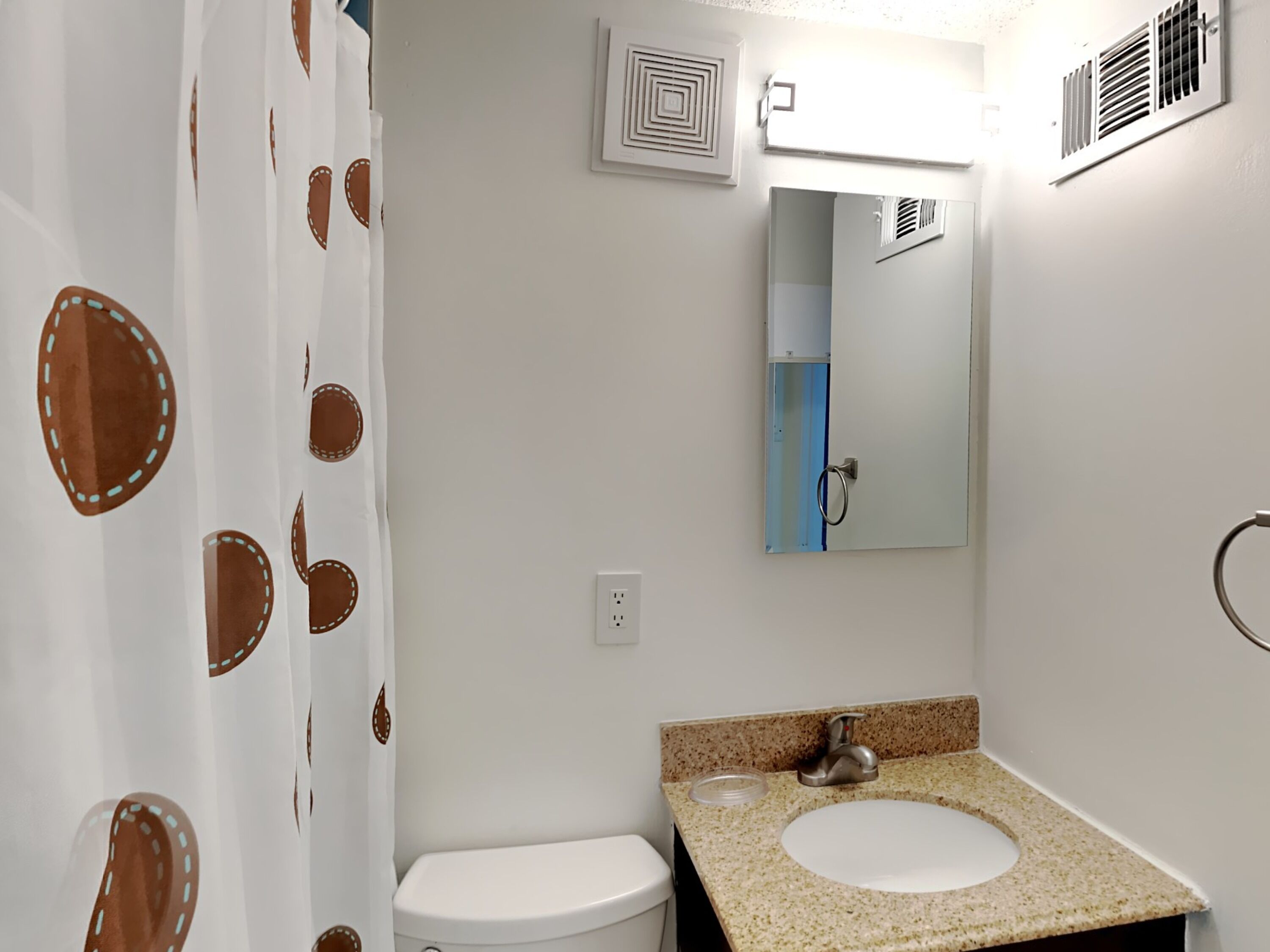 A bathroom with a toilet, sink, mirror, and shower curtain.
