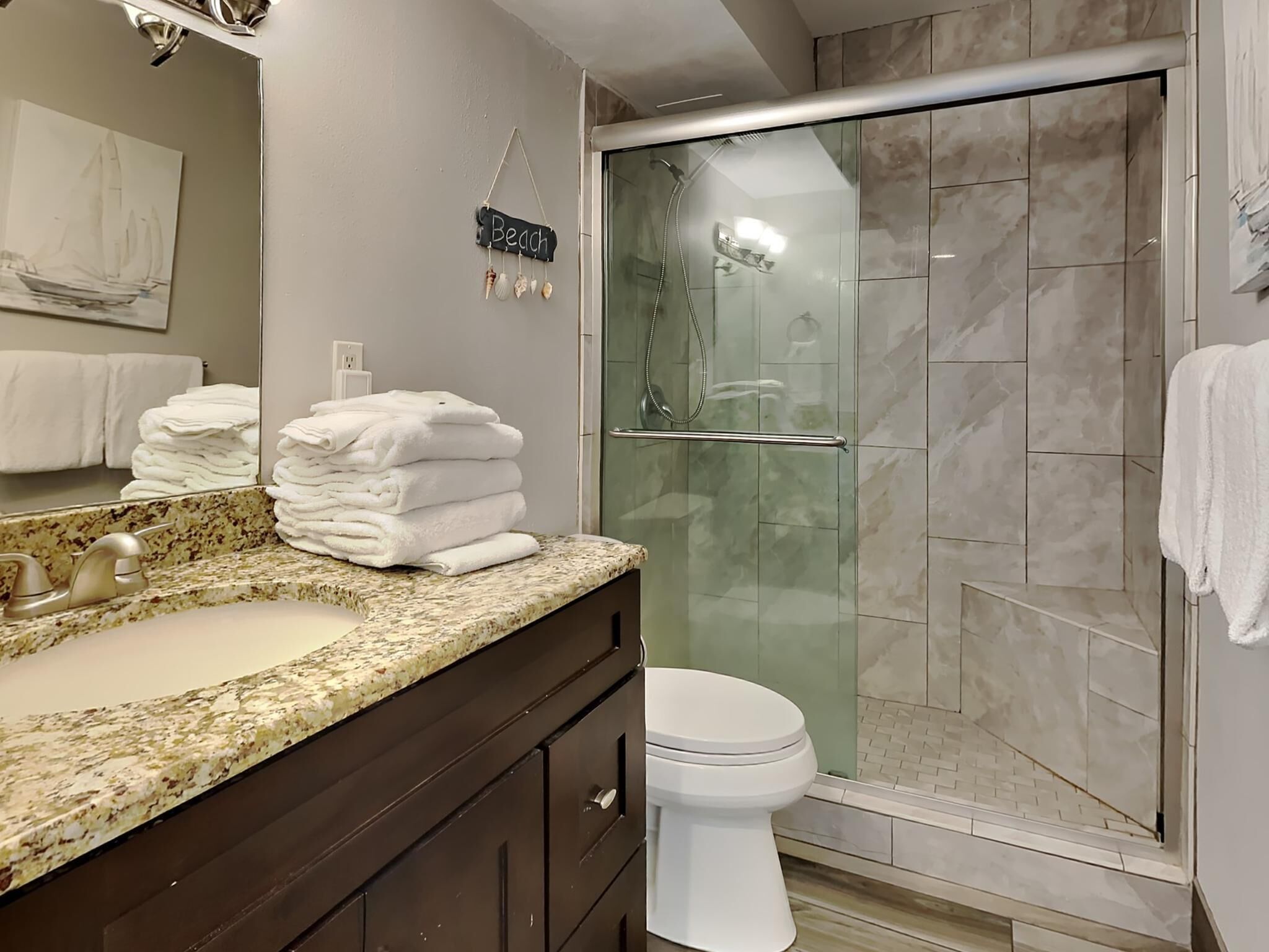 Une salle de bain dotée d’un comptoir en granit, d’un lavabo, de toilettes et d’une douche à parois de verre.
