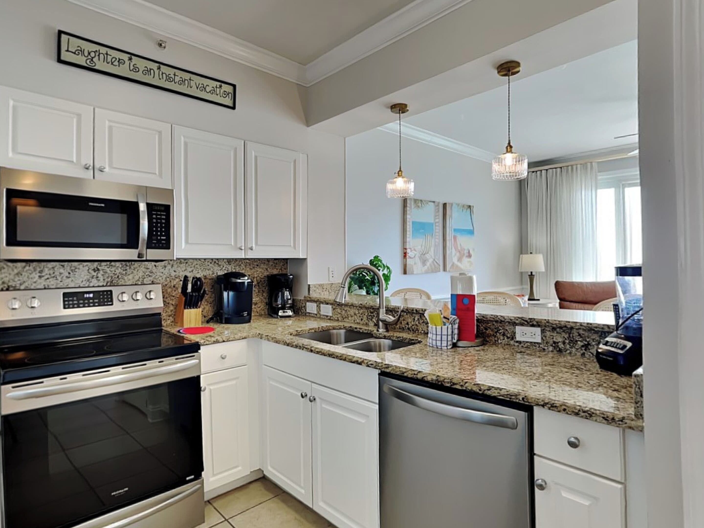 A modern kitchen with white cabinets, stainless steel appliances, granite countertops, and pendant lighting.