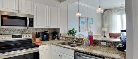 A modern kitchen with white cabinets, stainless steel appliances, granite countertops, and pendant lighting.