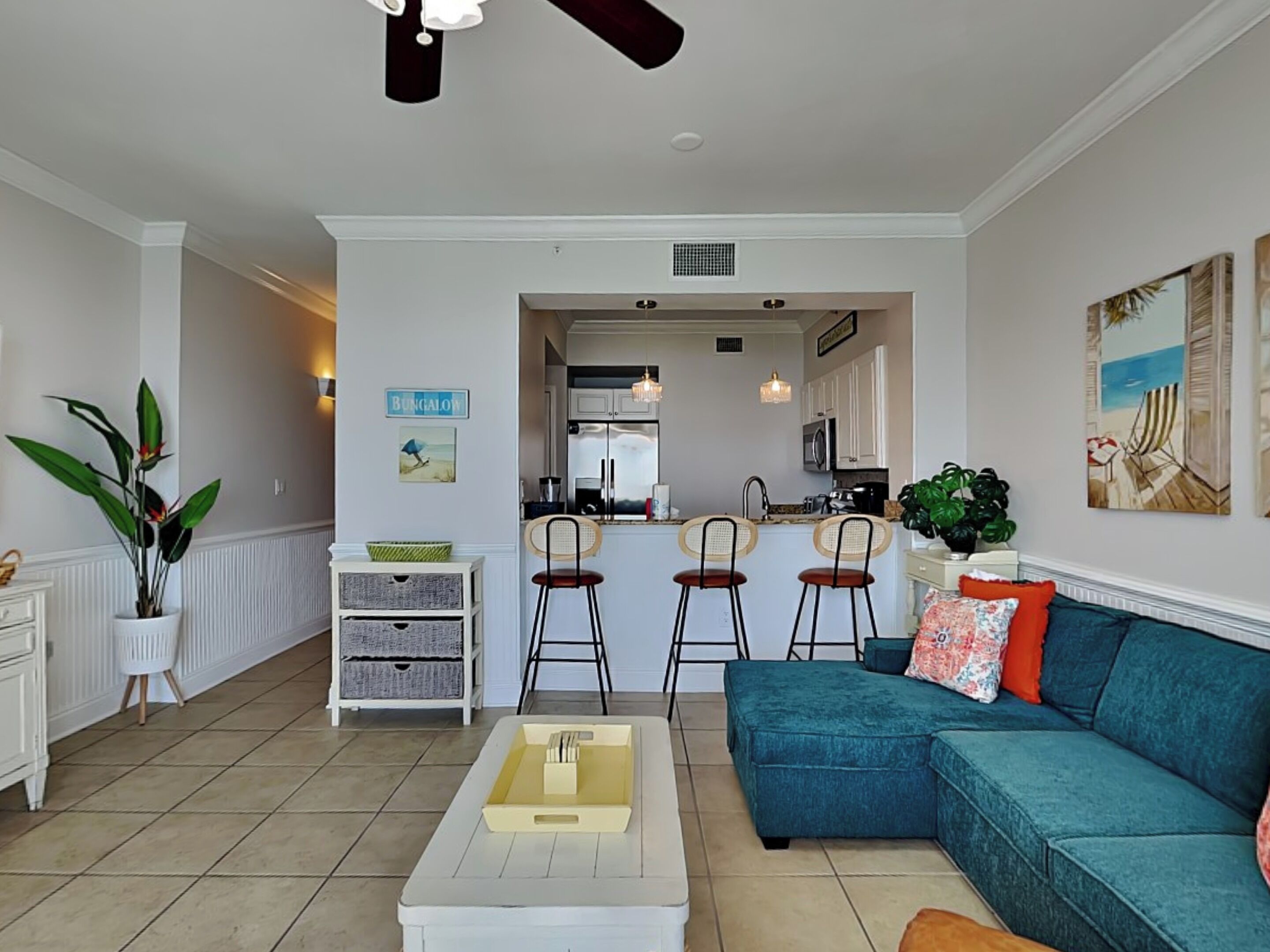 Una sala moderna con un sofá azul verdoso, una mesa de centro blanca y una cocina con armarios blancos y un taburete de bar.