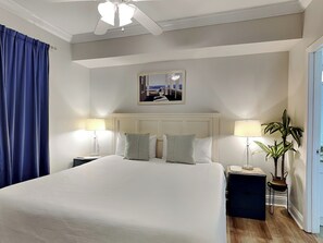Habitación de hotel con una cama grande, dos mesitas de noche, un ventilador de techo, un cuadro en la pared y una planta en maceta.
