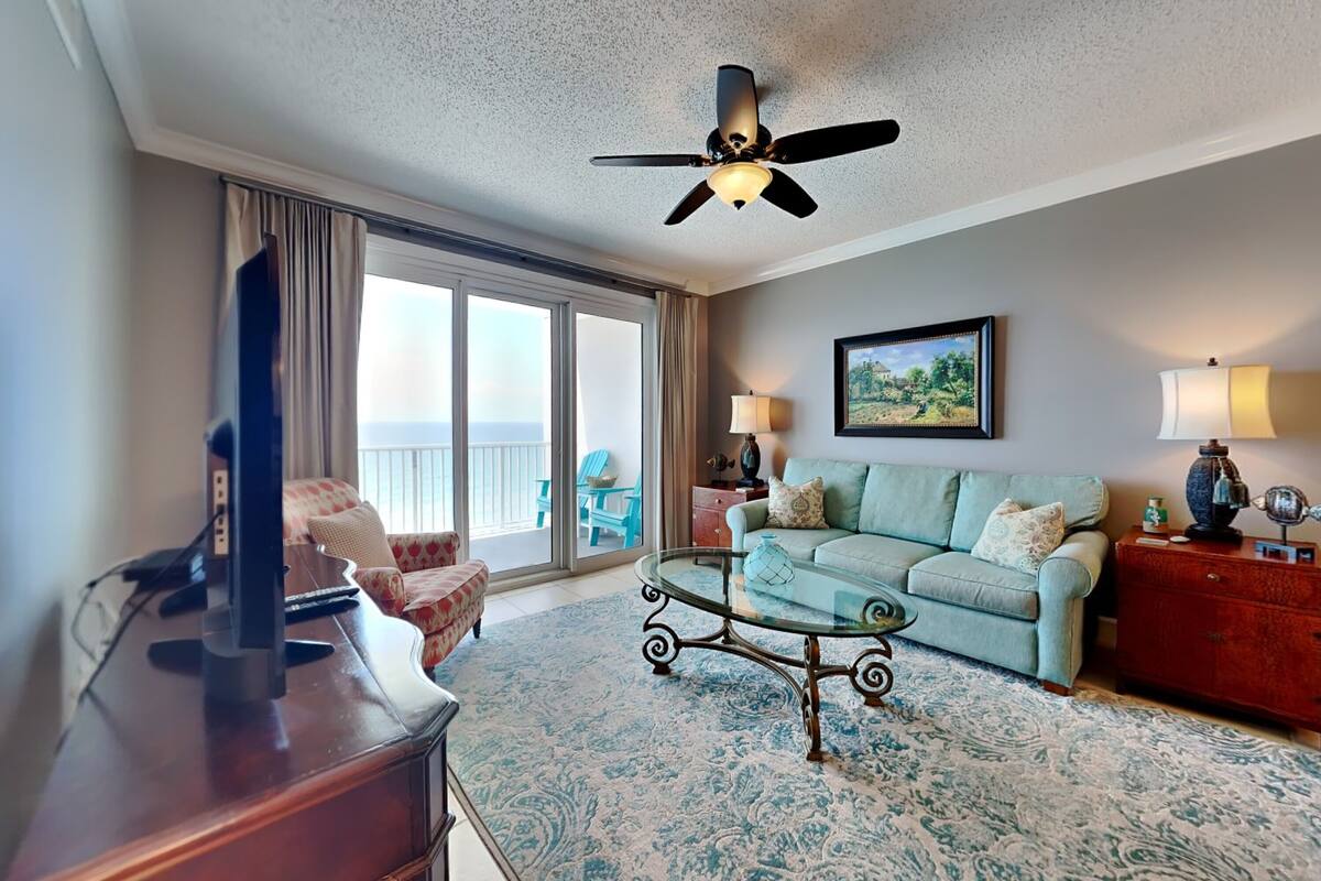 A living room with a large window, a ceiling fan, a sofa, a coffee table, and a TV.