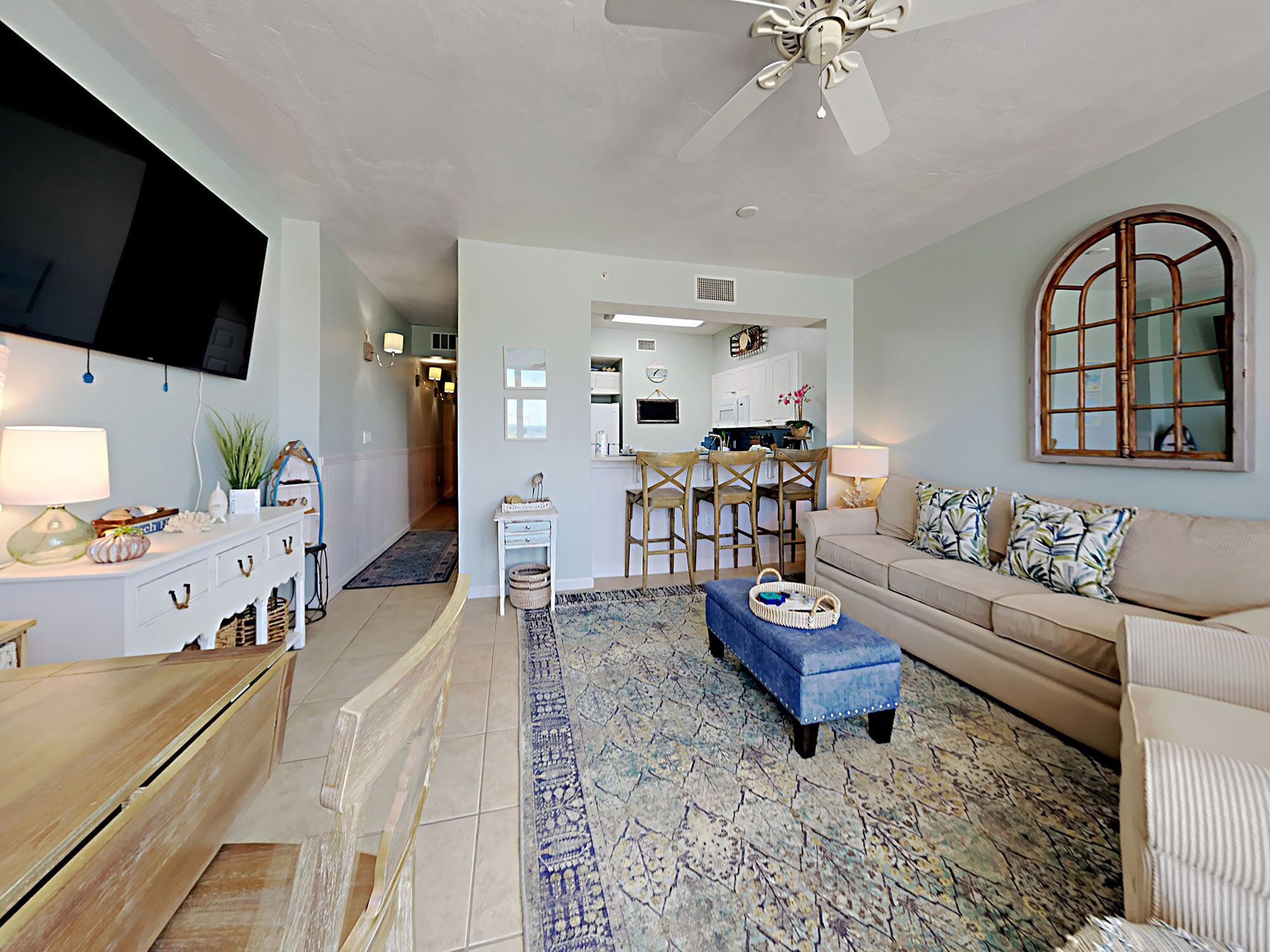 A living room with a TV, sofa, and coffee table. There is a kitchen in the background with a dining area.
