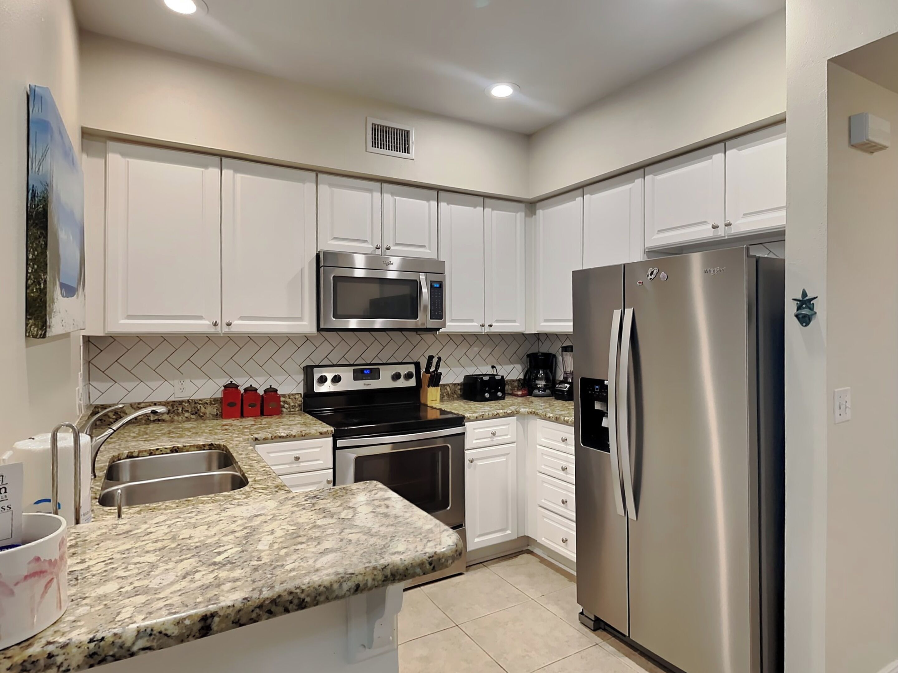 A modern kitchen with white cabinets, stainless steel appliances, granite countertops, and a tiled backsplash.